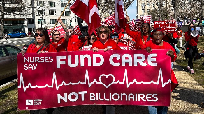 California nurses dressed in all red hold a red banner that reads Fund Care Not Billionaires